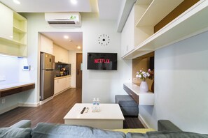 Ein modernes Wohnzimmer mit einer Couch, einem Couchtisch, einem Fernseher, der 'NETFLIX' anzeigt, und einer Küche im Hintergrund.