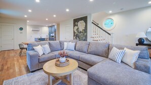 A modern living room with a grey sectional sofa, a round wooden coffee table, and a kitchen in the background. - LUX Waterside Retreat with Geo Dome + Outdoor Fire Table, Historic Property (Prospect)
