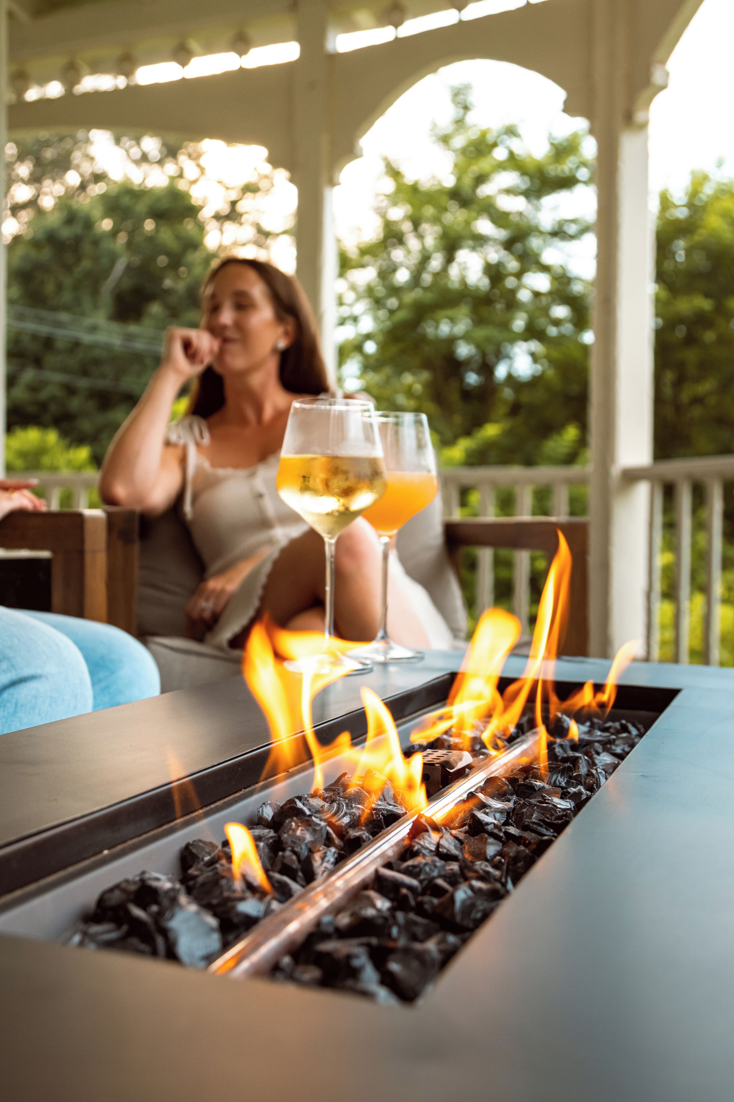 Una chimenea con vasos de bebidas, un banco de madera y una zona de estar al aire libre techada.