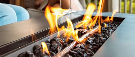 A fire feature with glasses of beverages, a wooden bench, and a covered outdoor seating area.