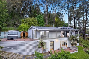Uma casa moderna com um alpendre amplo, uma banheira de hidromassagem e uma sauna de madeira.