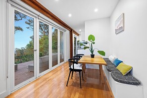 Uma sala de jantar moderna com uma mesa de madeira, cadeiras pretas e um banco com almofadas coloridas.