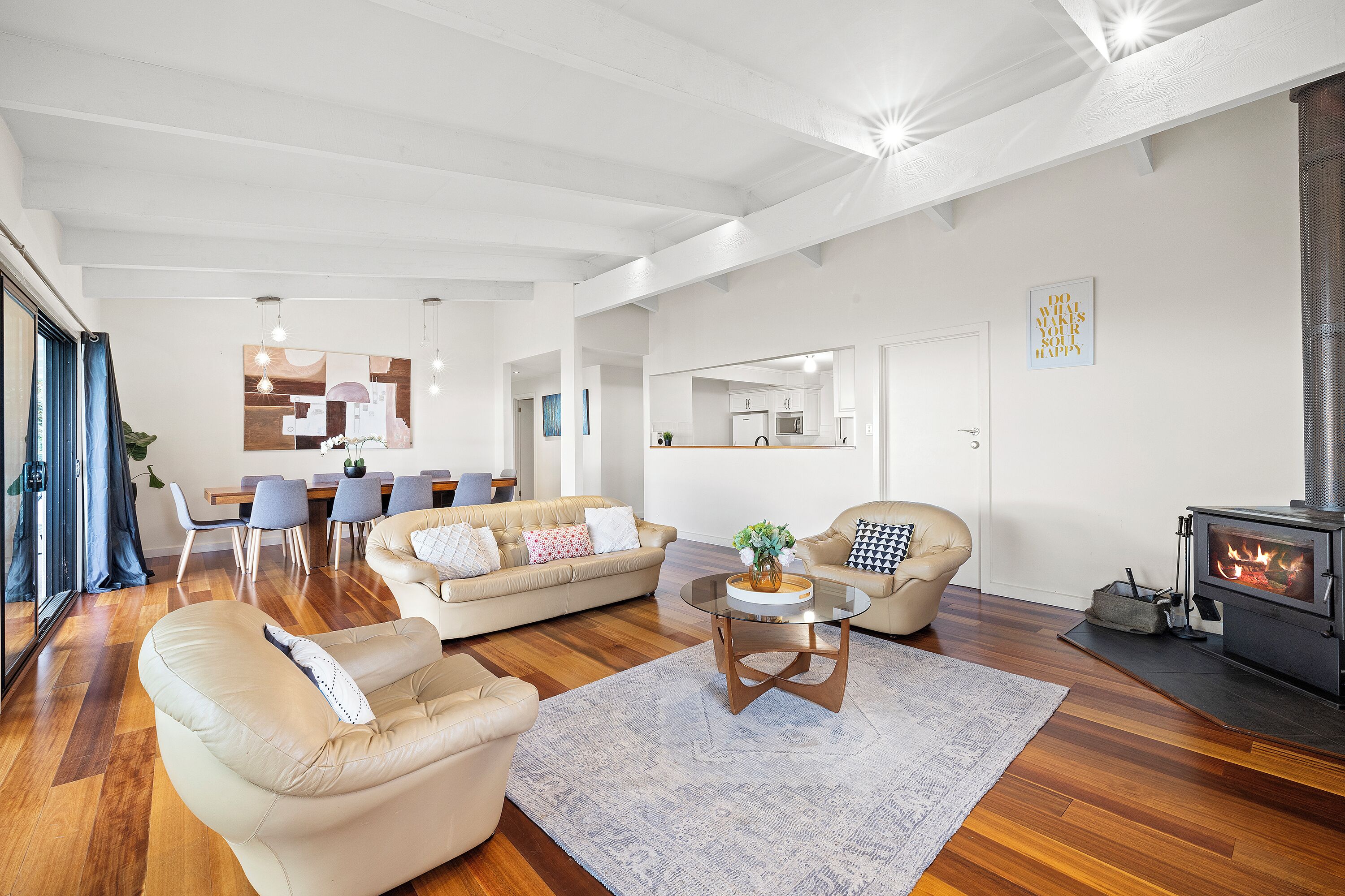 A modern living room with a sofa, armchair, and a coffee table. There is a dining area with chairs and a table, and a kitchen in the background.