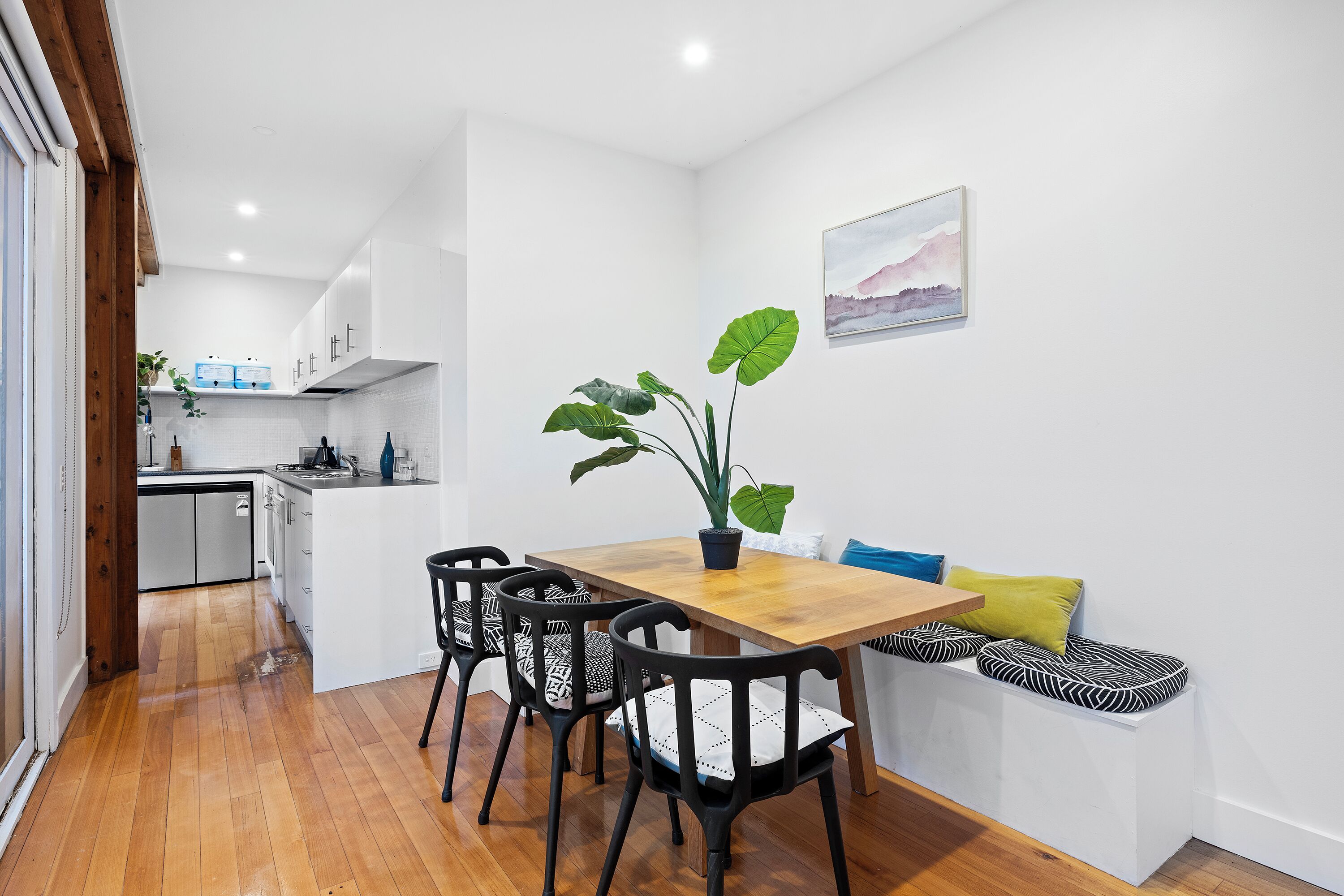 Una cocina compacta con armarios blancos, una mesa de comedor de madera y sillas negras.