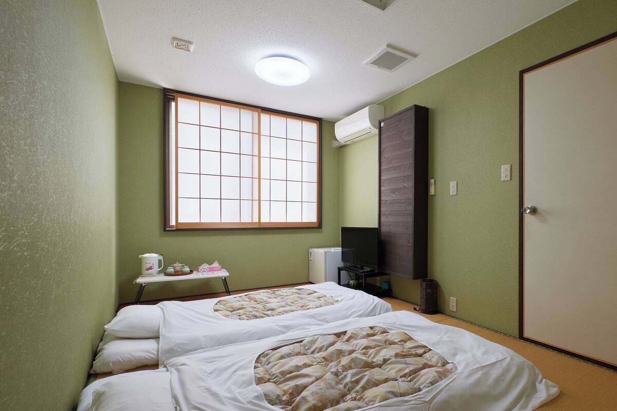 A room with two beds, a window, a television, and a small table with a kettle and cups.