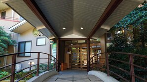 A covered walkway leading to a building with a wooden railing and a stone floor. - Tabist Sakura no Yakata Hotel (Fuefuki)