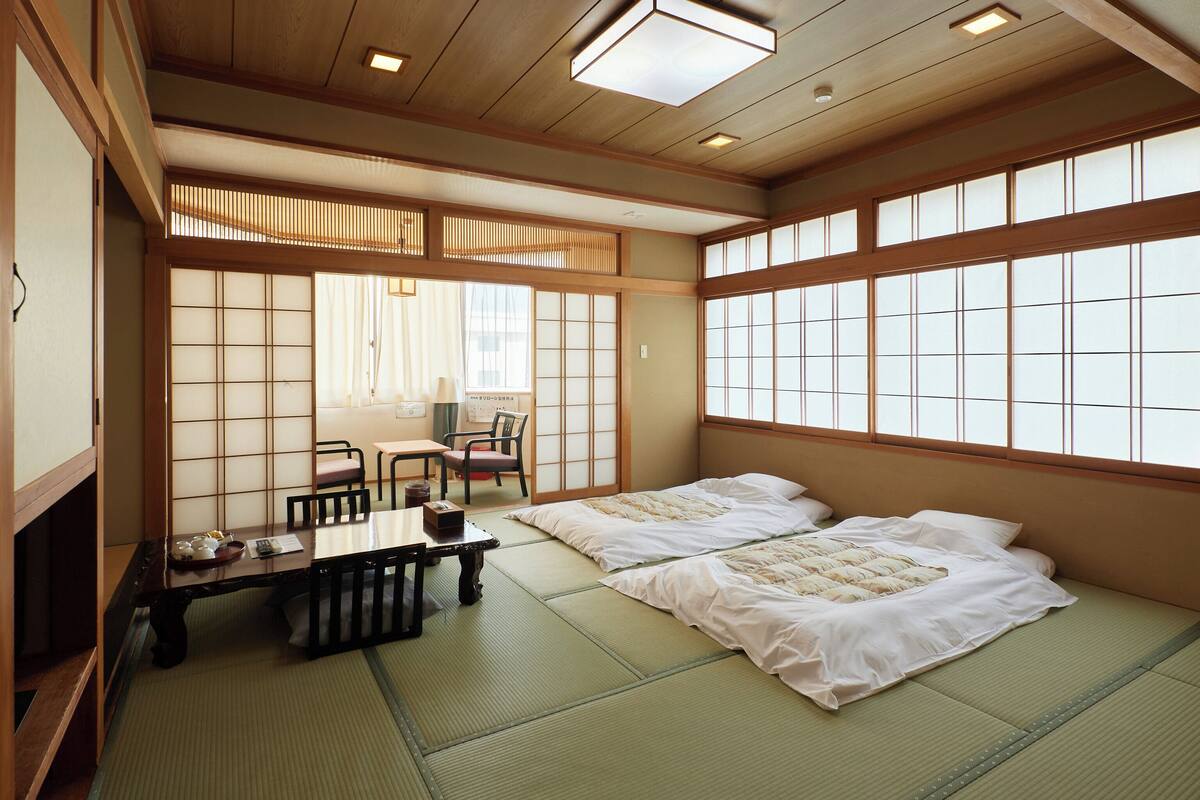 A traditional Japanese room with tatami flooring, two beds, a low table with a tea set, and sliding doors.