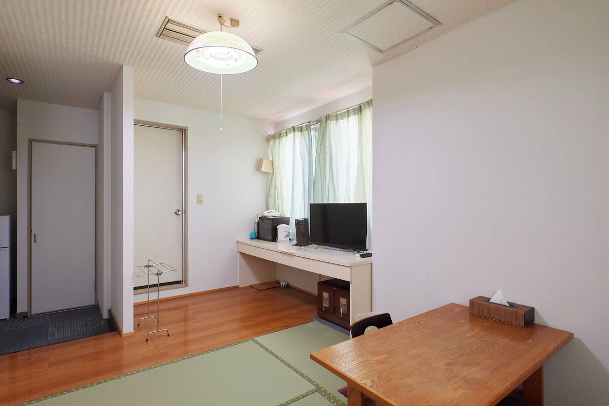 A room with a wooden desk, a television, a lamp, and a small table.