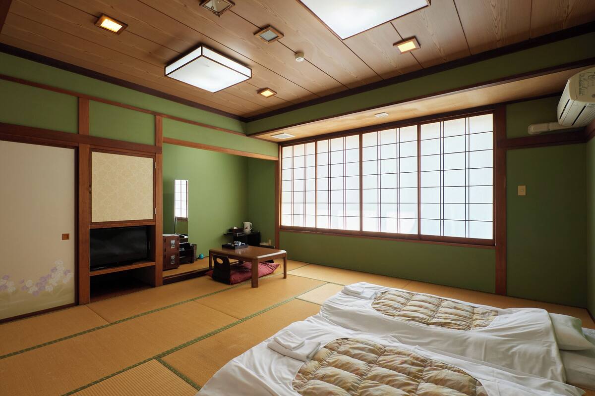 A traditional Japanese room with tatami flooring, a futon bed, a television, and sliding doors.