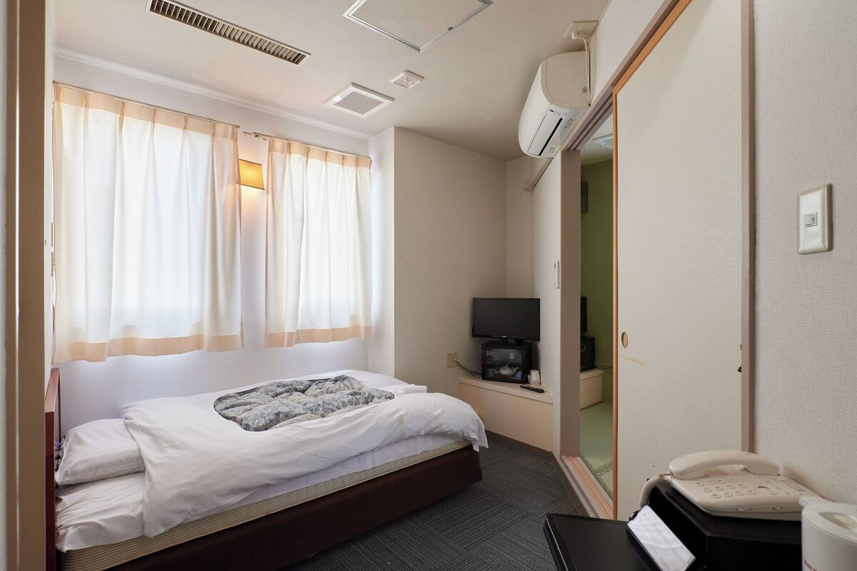 A hotel room with a bed, a television, a telephone, and an air conditioning unit.