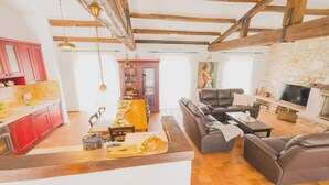A spacious living area with a sofa set, a dining table with chairs, a kitchen with red cabinets, and a stone fireplace. - Jurinea in Vi Njan With 4 Bedrooms and 2 Bathrooms (Visnjan)