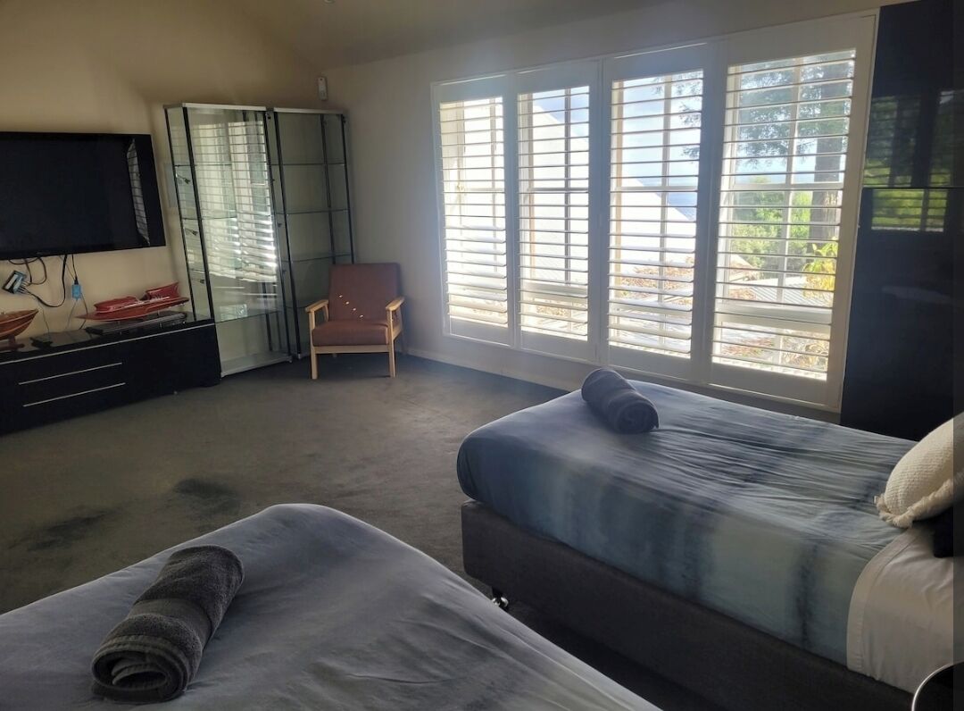 A hotel room with two beds, a TV, a chair, and large windows.