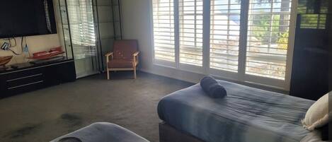 A hotel room with two beds, a TV, a chair, and large windows.