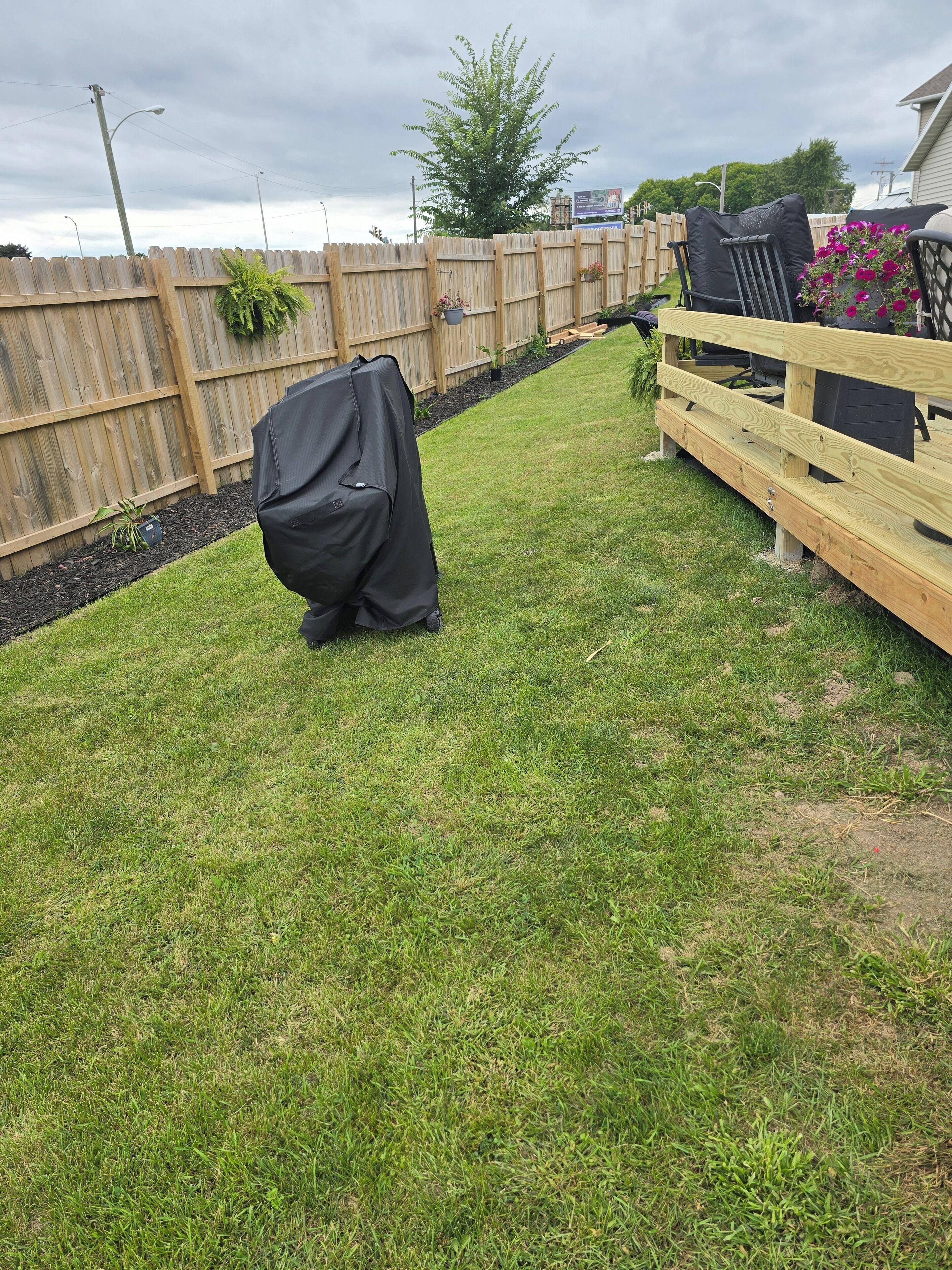 A backyard with a wooden fence, a covered grill, and a wooden deck.