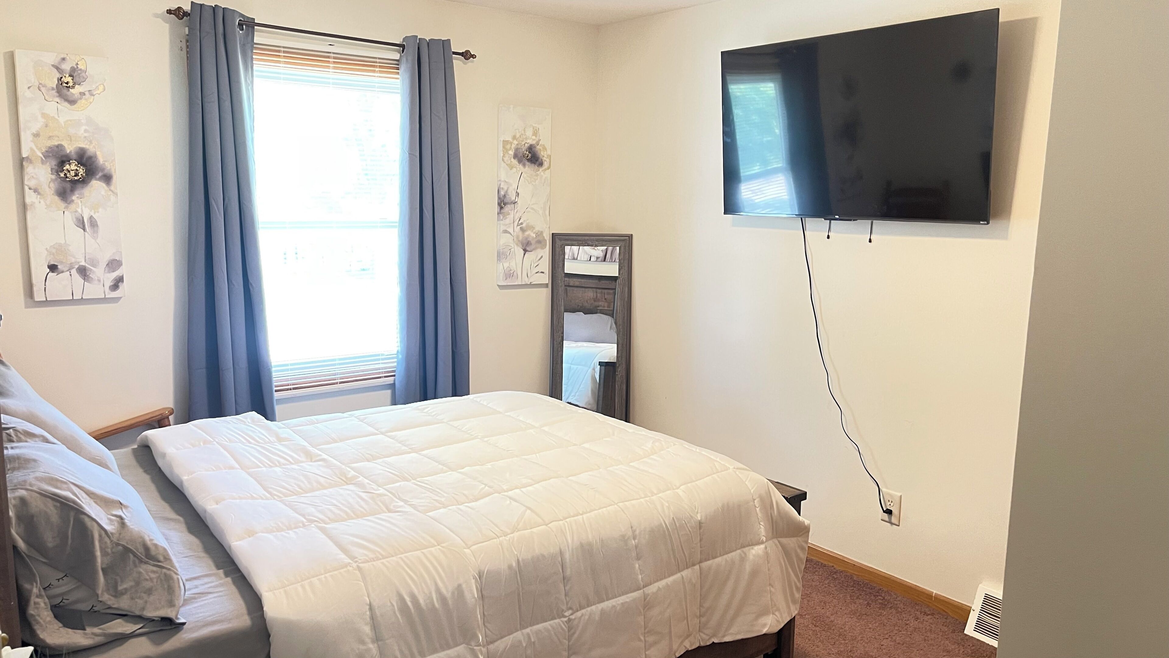 A bedroom with a bed, a flat-screen TV mounted on the wall, and artwork on the walls.