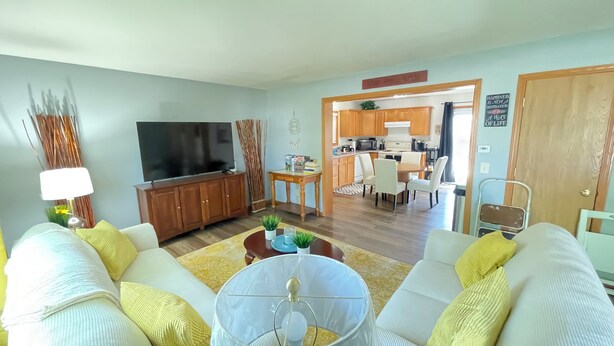 A living room with a TV, sofa, and coffee table. There is a dining area with chairs and a table. A kitchen is visible in the background. - Beautiful 3br, 1.5 bath townhouse centrally located in the heart of Milwaukee. (Milwaukee)