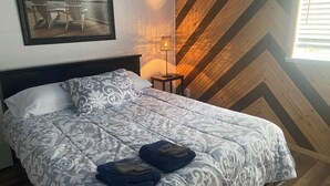 A neatly made bed with a patterned bedspread, a framed picture on the wall, and a lamp beside the bed.