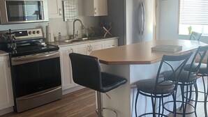 A modern kitchen with white cabinets, stainless steel appliances, a wooden ceiling, and a bar area with black stools.