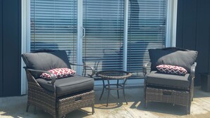 A patio with two wicker chairs and a small table, a sliding glass door, and a dark exterior wall.