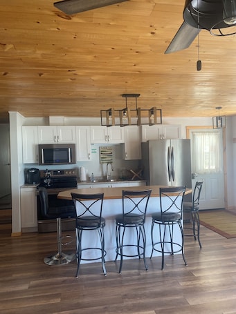 A modern kitchen with white cabinets, stainless steel appliances, and a wooden ceiling.