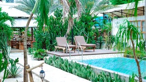 A pool area with two lounge chairs, surrounded by various tropical plants and a stone wall.