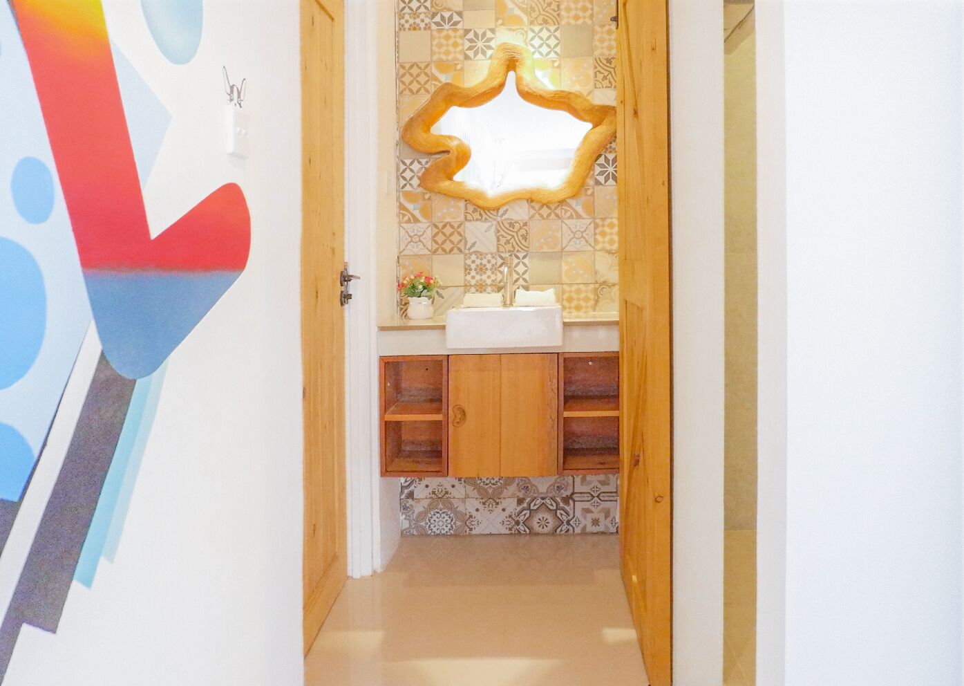 Un couloir étroit mène à une salle de bain dont le mur derrière le lavabo est recouvert de carreaux, qui comprend également un meuble en bois et un miroir.