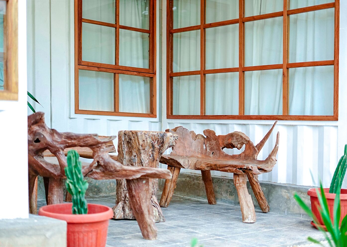 A wooden bench with a natural finish, positioned in front of a building with large windows and white trim.