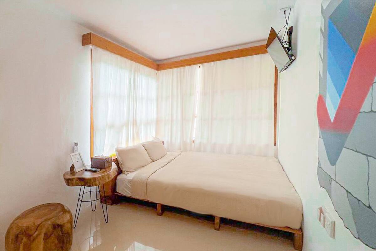 A bedroom with a bed, a small table, and a wall-mounted lamp.