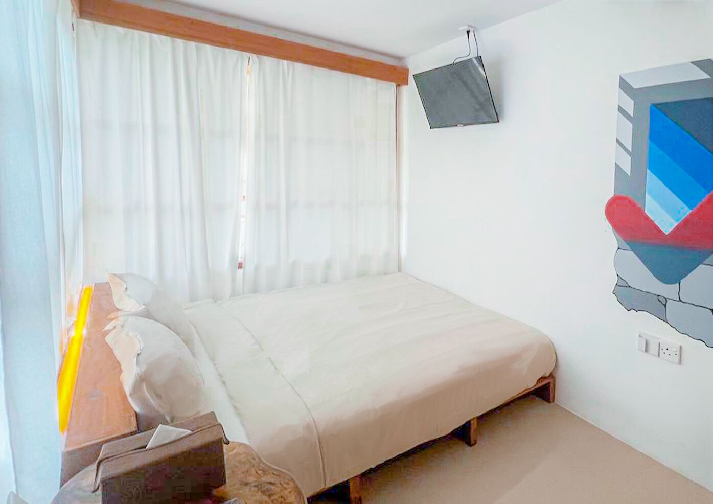 A bedroom with a bed, a TV mounted on the wall, and a window with curtains.