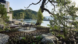 Un tranquilo espacio al aire libre con mesas y sillas, con vista a un lago sereno y abundante vegetación.