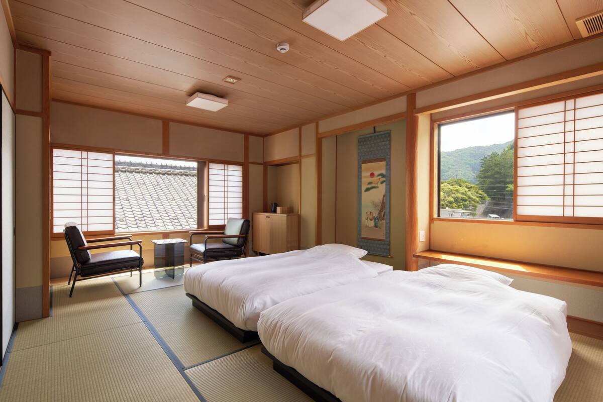 Ett traditionellt japanskt rum med tatamimattor på golvet, en stor säng, ett skrivbord och utsikt över ett berg genom skjutbara, genomskinliga dörrar (shoji).