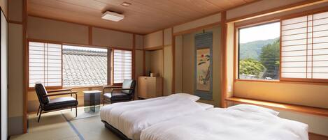 Quarto tradicional japonês, com tatames, uma cama grande, uma mesa e vista para uma montanha através de biombos de papel.