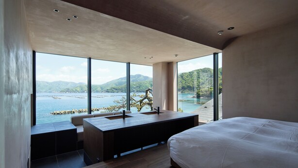 Un dormitorio moderno con una cama grande, un escritorio de madera con un lavamanos y vistas a un lago y montañas.