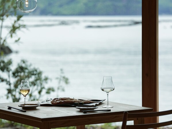 A wooden table with two glasses of white wine, a plate with food, and chopsticks.