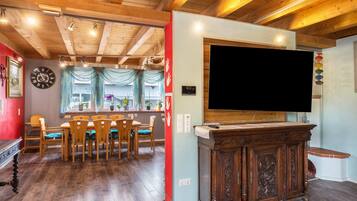 Zona pranzo con sedie di legno e un tavolo, una TV su un mobile in legno e una sveglia appesa al muro.