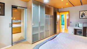 Un dormitorio con cama, armario de puertas de cristal, escritorio con ordenador y puerta que da a otra habitación.