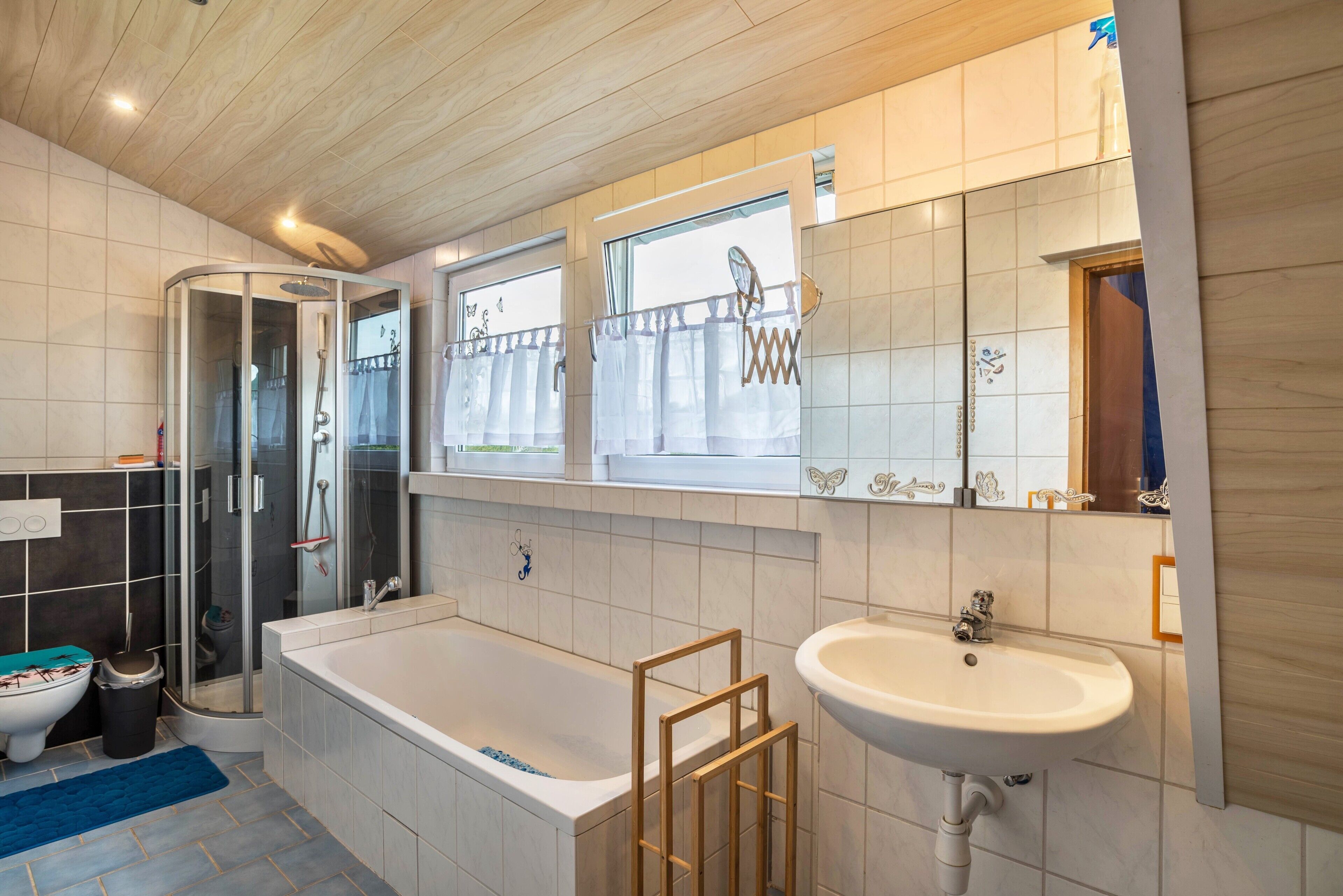 A modern bathroom with a glass-enclosed shower, a bathtub, a sink, and a window with curtains.