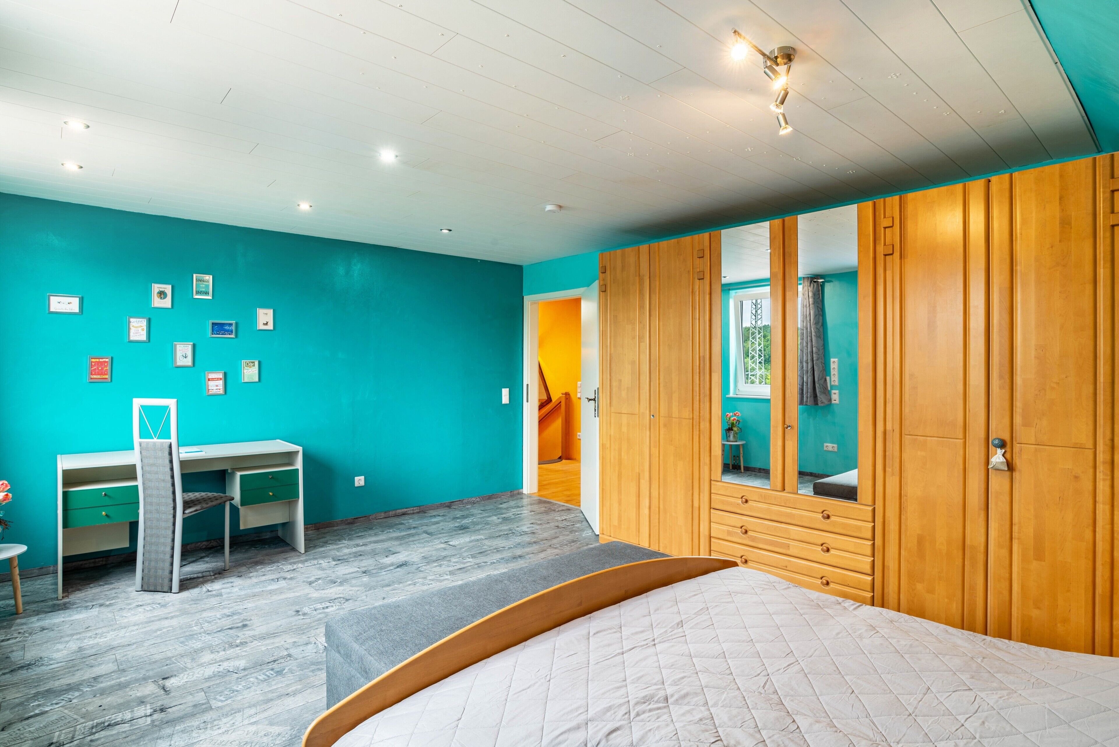 Une chambre avec des murs de couleur turquoise, une armoire en bois, un lit, un bureau et une chaise.