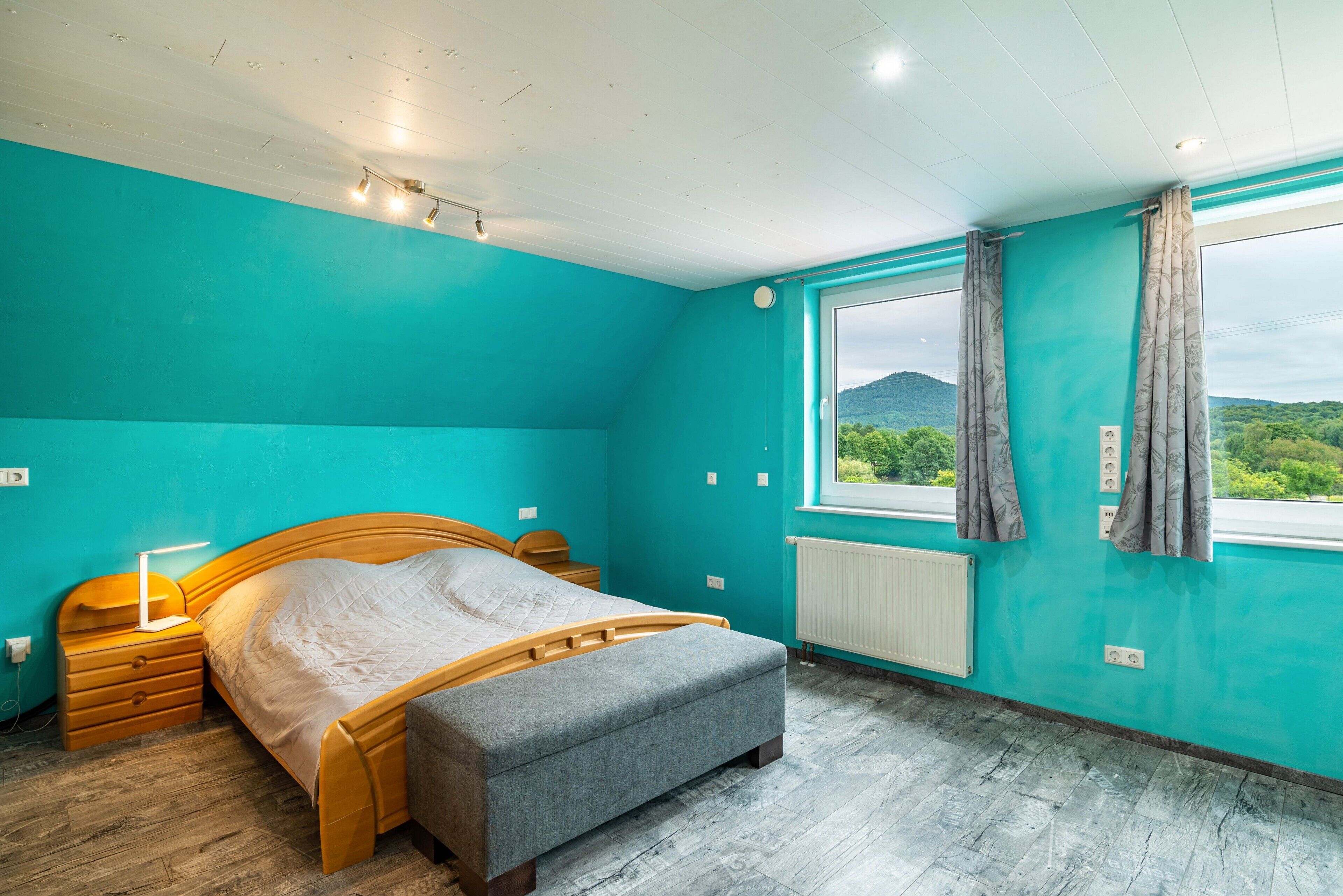 Ein Schlafzimmer mit Bett, Nachttischen, einem Fenster mit Vorhängen und Blick ins Grüne.