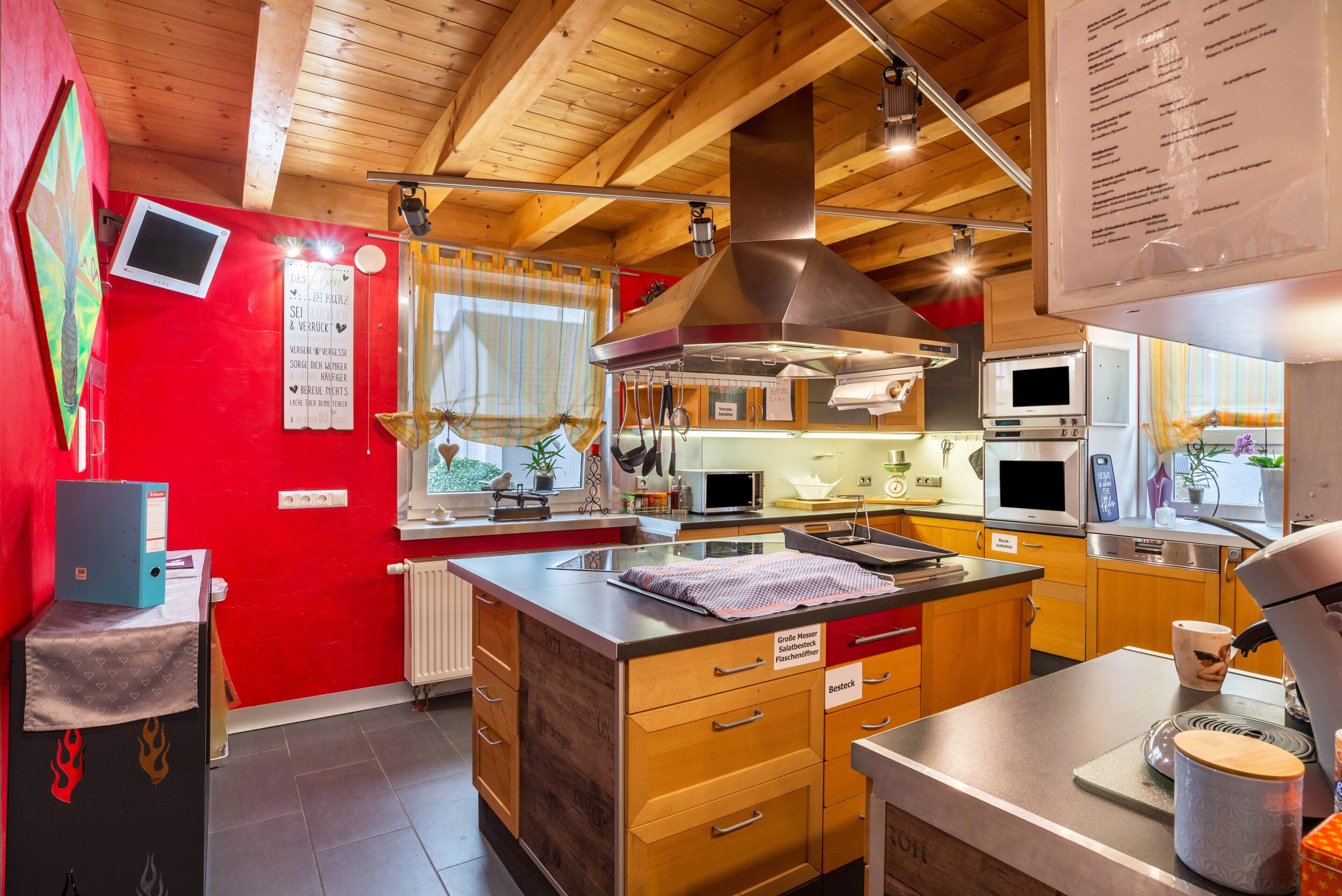 A modern kitchen with wooden cabinets, stainless steel appliances, and a red accent wall.
