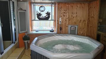 A hot tub in a room with wooden walls, a window with a decorative item, and a ceiling light fixture.