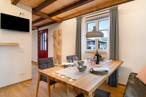Un coin repas comprenant une table en bois, des chaises, un téléviseur fixé au mur et une fenêtre avec des rideaux.
