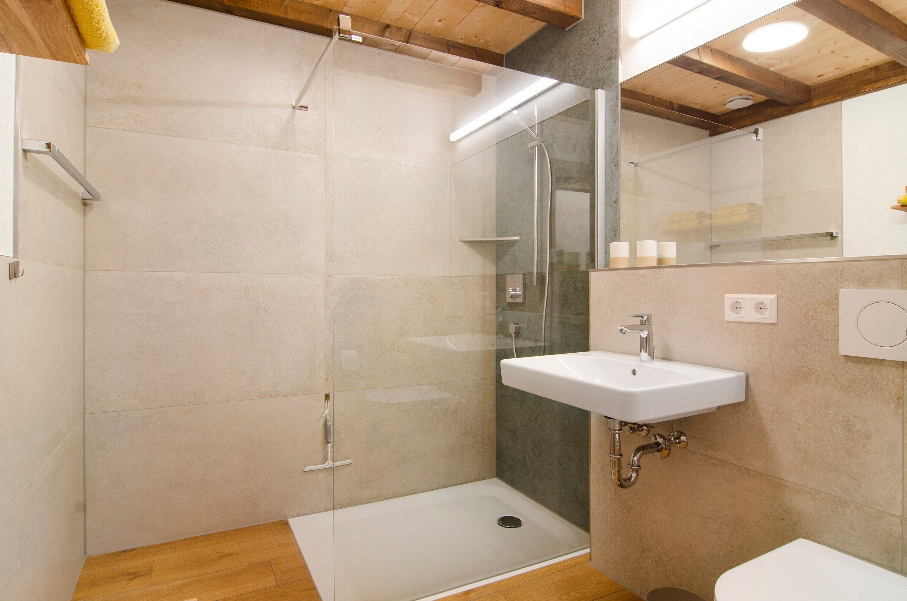 A modern bathroom with a glass shower enclosure, a white sink, and a wooden floor.