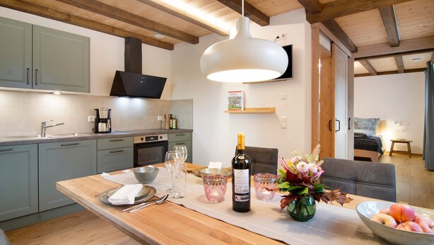 A modern kitchen with grey cabinets, a wooden ceiling, a large island with a bottle of wine, glasses, and a bowl of fruit. - Holiday Apartment "Morgentau" with Private Terrace & Wi-Fi (Heiligenberg)