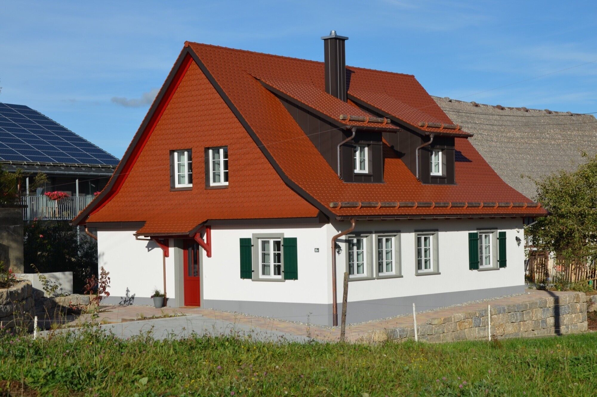 Ein zweistöckiges Haus mit rotem Dach, weißen Wänden und grünen Fensterläden.