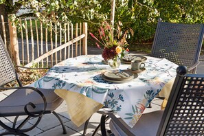 Un espace extérieur aménagé pour les repas, avec une table dressée pour deux personnes, entourée de chaises, et une clôture en bois en arrière-plan.