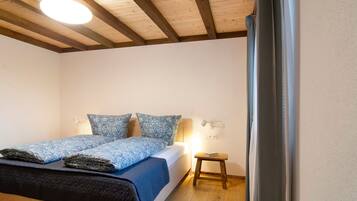 Quarto com cama, luminárias de cabeceira, um banquinho de madeira e luz no teto.