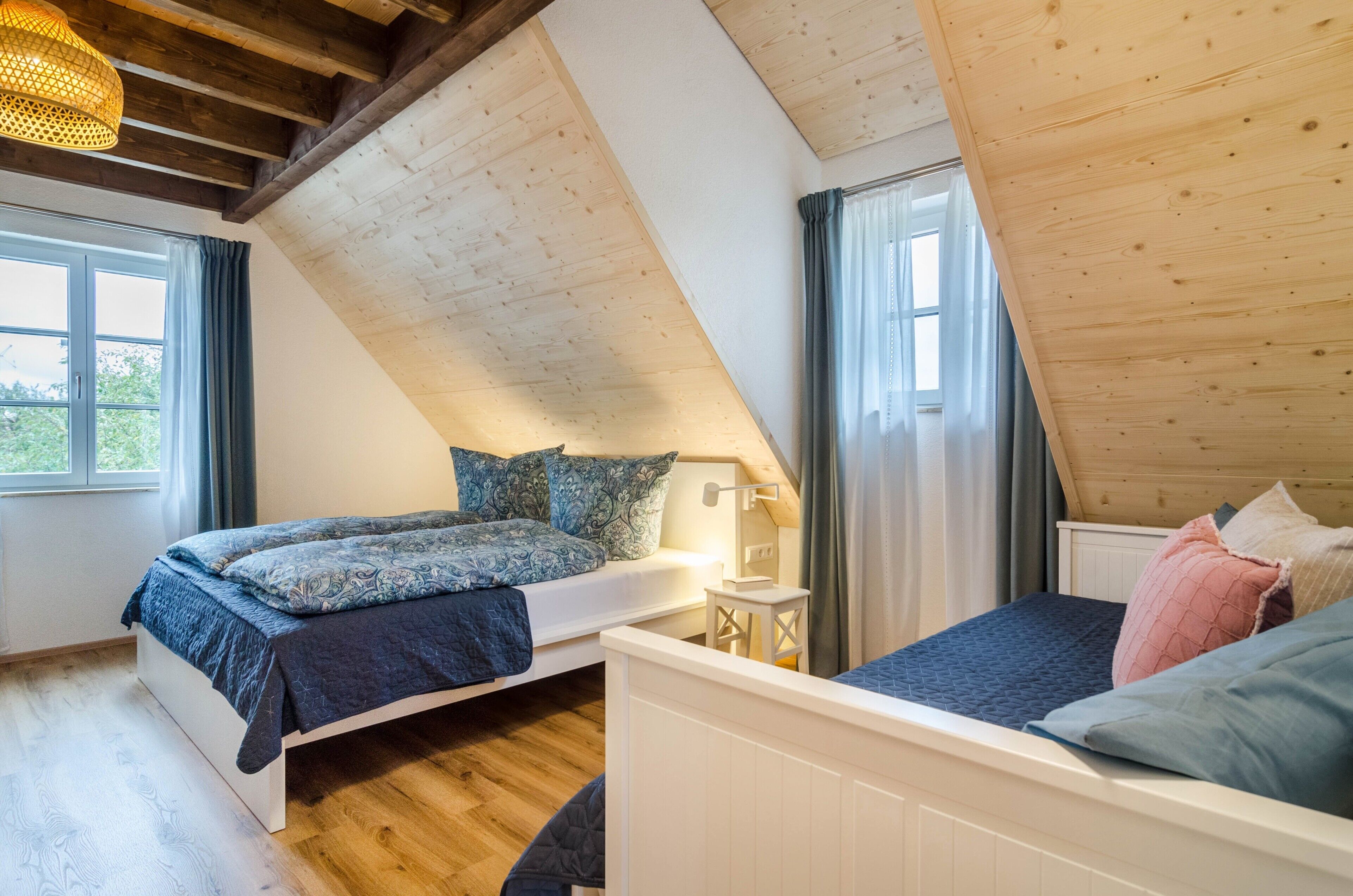 A bedroom with two beds, a window, and a wooden ceiling.