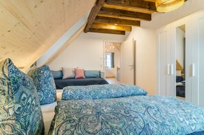 A bedroom with a sloped ceiling, a bed with patterned bedding, a window, and a wardrobe.