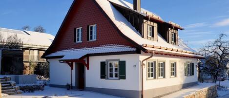 Ein zweistöckiges Haus mit einem steilen Dach, einem Schornstein und einer kleinen Veranda.